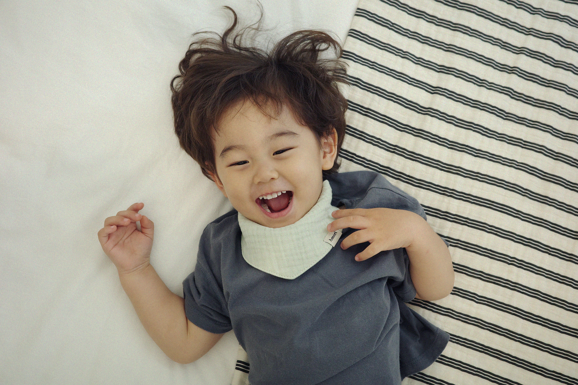 아모리 크림 거즈 스카프 빕 착용 아기 침대 위 웃는 모습